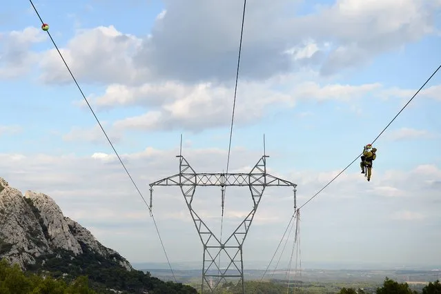 An electrician installs a marker on a high-tension line of 225 000 volts, on October 9, 2015, in Eygalieres, southern France. To prevent birds of prey colliding in high-tension lines, new luminescent markers, light enough for the steep areas, are installed in the Alpilles Regional Natural Park. (Photo by Boris Horvat/AFP Photo)