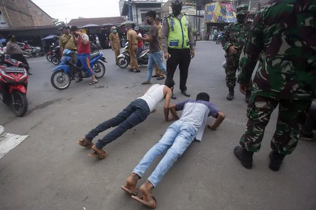 An Indonesian policeman and soldiers watch men do push-ups as a punishment for violating city regulation requiring people to wear face masks in public places as a precaution against coronavirus outbreak, in Medan, North Sumatra, Indonesia, Wednesday, September 23, 2020. (Photo by Binsar Bakkara/AP Photo)