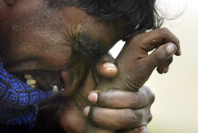 An Indian man cries as he holds the hand of his eight-year-old son who was killed in a tsunami in Cuddalore, south of the Indian city of Madras, in this December 27, 2004 file photo. (Photo by Arko Datta/Reuters)