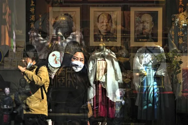 A woman wearing a face mask is reflected on a window panel as she walks by a fashion boutique selling Chinese traditional costumes at a tourist shopping street in Beijing, Wednesday, March 1, 2023. Chinese leader Xi Jinping's agenda for the annual meeting of the ceremonial legislature: Revive the struggling economy by encouraging consumers to spend now that severe anti-virus controls have ended. Install a government of Xi loyalists to intensify the ruling Communist Party's control over the economy and society. (Photo by Andy Wong/AP Photo)
