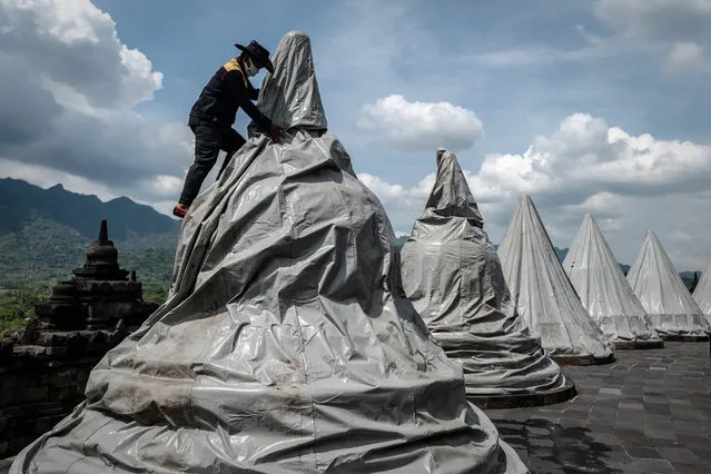 A worker covers a statue to prevent damage from volcanic ash at Borobudur temple on November 12, 2020 in Magelang, Central Java, Indonesia. Workers rushed to cover statues and religious structures at the ninth-century temple, a UNESCO World Heritage site, to prevent damage from volcanic ash as Mount Merapi showed renewed signs of activity. (Photo by Ulet Ifansasti/Getty Images)