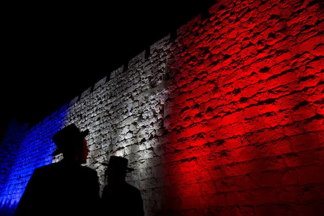 Two Ultra-Orthodox Jews look at Jerusalem's Old City walls illuminated by the colors of the French national flag in solidarity with France after attacks in Paris, in Jerusalem, Sunday, November 15, 2015. (Photo by Ariel Schalit/AP Photo)