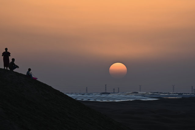 This picture taken on August 10, 2025 shows the sun setting over solar panels at the Dalat Banner Photovoltaic Station , also known as the Junma, or “Fine Horse”, Solar Power Station, in the Kubuqi desert near Ordos, in China's northern Inner Mongolia region. An ocean of blue solar panels ripples across the ochre dunes of Inner Mongolia's Kubuqi desert, a glittering example of China's mammoth energy transition efforts in action. Even as other countries have put the brakes on desert solar projects for economic or technical reasons, China – the world's largest emitter of greenhouse gases – is still ploughing ahead. (Photo by Pedro Pardo/AFP Photo)