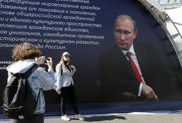 A woman has her picture taken in front of a portrait of the Russian President Vladimir Putin during a book fair on the Dvortsovaya (Palace) Square in St. Petersburg, Russia, 19 May 2023. (Photo by Anatoly Maltsev/EPA/EFE)