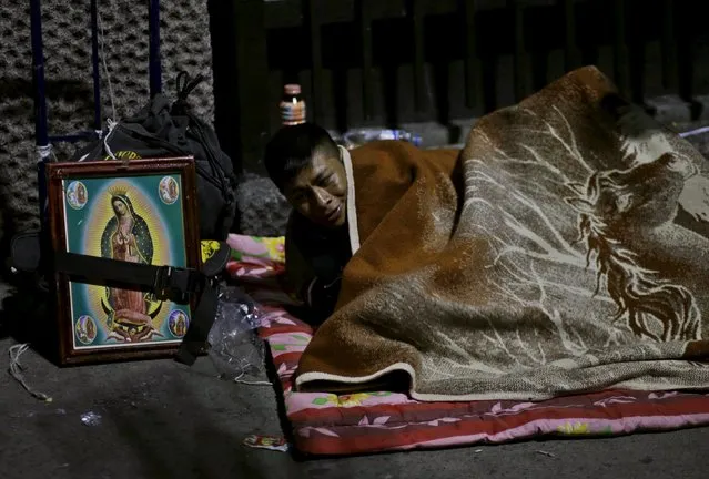 A pilgrim rests beside an image of the Virgin of Guadalupe next to an improvised camp site outside the Basilica of Guadalupe during the annual pilgrimage in honor of the Virgin of Guadalupe, patron saint of Mexican Catholics, in Mexico City, Mexico December 11, 2015. (Photo by Henry Romero/Reuters)