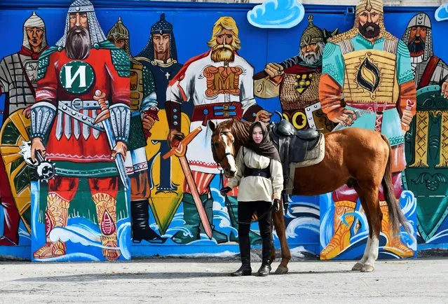 A woman stands with a horse next to a graffiti during celebrations of the Defender of the Fatherland Day in Vladivostok, Russia on February 23, 2021. (Photo by Yuri Maltsev/Reuters)