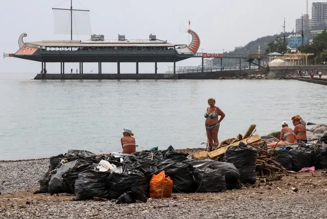 People sit on a beach next to garbage brought by flooding after heavy rainfall in Yalta, Crimea on June 22, 2021. (Photo by Alexey Pavlishak/Reuters)