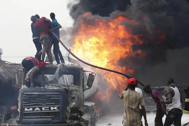 People help firefighters try to contain a fire at a petrol station in Lagos, Nigeria on Thursday, March 26, 2015. Witnesses said no one was injured in the fire that consumed a number of trucks  and cars at the site. Authorities continue to investigate what caused the blaze. (Photo by Sunday Alamba/AP Photo)