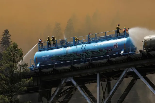 Firefighters spray water from a fire train to hot spots along the tracks over Rock Creek Bridge as the Dixie Fire grows in Plumas National Forest, California, U.S., July 15, 2021. (Photo by David Swanson/Reuters)
