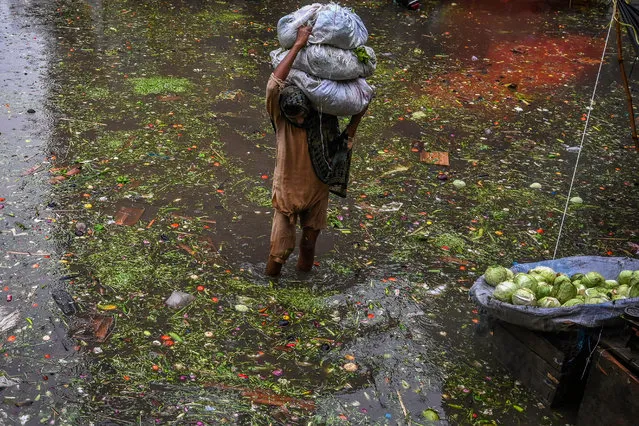 A worker carries vegetables as he wades through a waterlogged street along a market area during heavy monsoon rains in Lahore on July 20, 2021. (Photo by Arif Ali/AFP Photo)