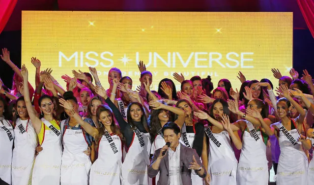 Miss Universe contestants raise their hands as Filipino singer Gerald Santos, center, sings before helping charitable organizations pack meals for distribution to the needy in suburban Pasay city southeast of Manila, Philippines Wednesday, January 18, 2017. (Photo by Bullit Marquez/AP Photo)