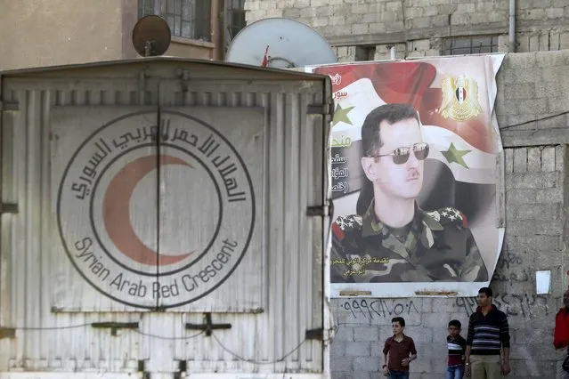An aid convoy of the Syrian Arab Red Crescent enters the Wafideen Camp, which is controlled by Syrian government forces, near a poster of Syria's president Bashar al-Assad, to deliver aid into the rebel-held besieged Douma neighborhood of Damascus, Syria March 4, 2016. (Photo by Omar Sanadiki/Reuters)