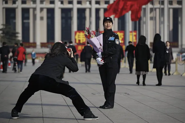 A woman takes a photo of a female police officer holding a bouquet of flowers on Tiananmen Square to mark International Women's Day during a plenary session of China's National People's Congress (NPC) at the Great Hall of the People in Beijing, Friday, March 8, 2019. (Photo by Andy Wong/AP Photo)