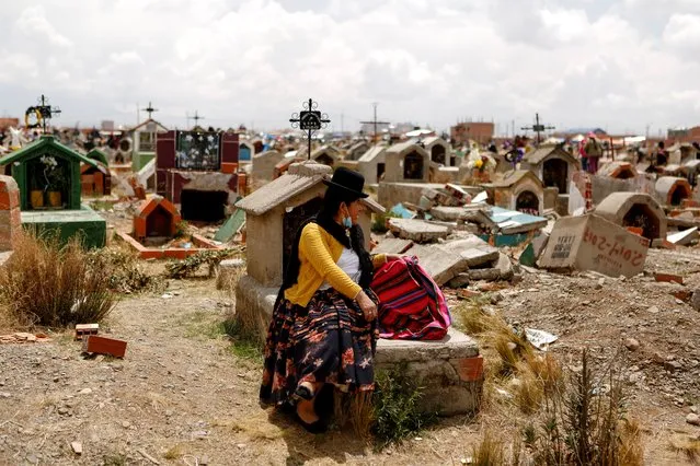 A woman sits on a grave at the Mercedario graveyard as she observes the Day of the Dead celebration, in El Alto, on the outskirts of La Paz, Bolivia, November 2, 2021. (Photo by Manuel Claure/Reuters)