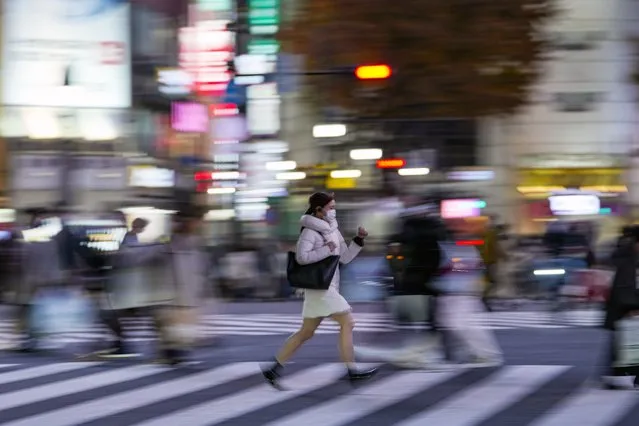 People wearing protective masks walk around the famed Shibuya scramble crossing in a shopping and entertainment district Monday, November 29, 2021, in Tokyo. (Photo by Kiichiro Sato/AP Photo)