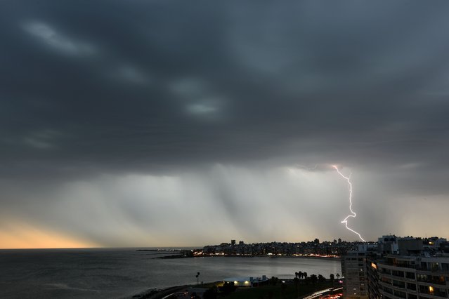 A lightning bolt is seen in a rain curtain during a storm over Montevideo on November 7, 2023. (Photo by Mariana Suarez/AFP Photo)