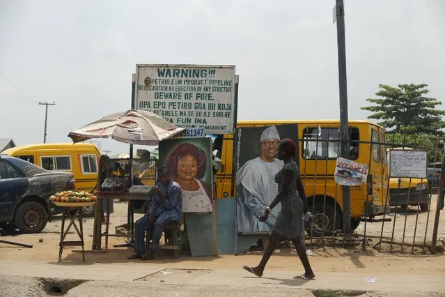 A woman walks past a portrait of Nigeria's President Muhammadu Buhari placed near a signboard campaigning against oil theft, along a road in Agege district in the commercial capital Lagos April 19, 2016. (Photo by Akintunde Akinleye/Reuters)