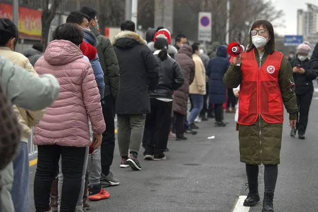 In this photo released by Xinhua News Agency, a volunteer wearing a face mask to protect from the coronavirus uses a loud speaker to give advise to masked residents as they line up for the coronavirus test during a mass testing in north China's Tianjin municipality, Sunday, January 9, 2022. Tianjin, a major Chinese city near Beijing has placed its 14 million residents on partial lockdown after 41 children and adults tested positive for COVID-19, including at least two with the omicron variant. (Photo by Sun Fanyue/Xinhua via AP Photo)