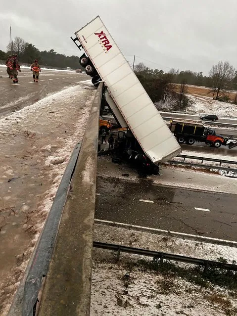In this photo provided by the Durham Police Department, a truck hangs from the highway N.C. 147 overpass after its cab apparently slid off the highway during winter weather, Sunday, January 16, 2022, in Durham, N.C. The cab of the truck appeared to have landed upright on Highway 15-501 below, while the trailer was in a vertical position, from the bridge to the highway below, causing road closures. (Photo by Durham Police Department via AP Photo)