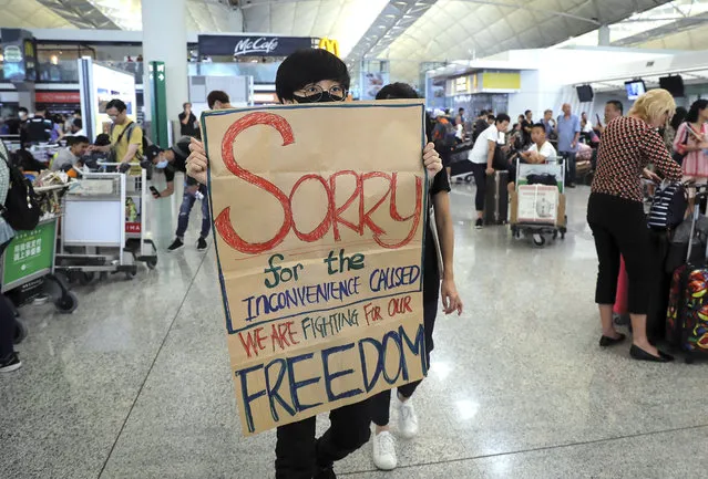 A protester shows a placard to stranded travelers during a demonstration at the Airport in Hong Kong, Tuesday, August 13, 2019. Protesters severely crippled operations at Hong Kong's international airport for a second day Tuesday, forcing authorities to cancel all remaining flights out of the city after demonstrators took over the terminals as part of their push for democratic reforms. (Photo by Kin Cheung/AP Photo)