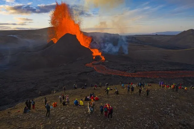 People watch as lava flows from an eruption from the Fagradalsfjall volcano on the Reykjanes Peninsula in southwestern Iceland on Tuesday, May 11, 2021. The glow from the bubbling hot lava spewing out of the Fagradalsfjall volcano can be seen from the outskirts of Iceland's capital, Reykjavík, which is about 32 kilometers (20 miles) away. Pandemic or no pandemic, the world will never stand still. That's perhaps no clearer than in Iceland where the Fagradalsfjall volcano has awoken from a slumber that has lasted 6,000 years, give or take a year or two. (Photo by Miguel Morenatti/AP Photo)