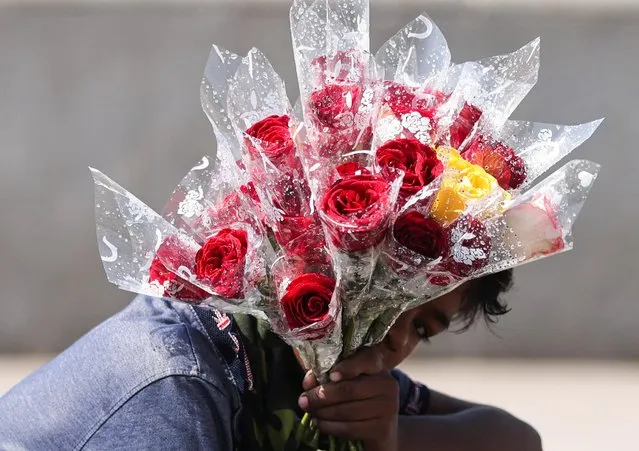 A boy shields his face from the sun with roses, as he waits for customers on Valentine's Day at a promenade in Mumbai, India, February 14, 2022. (Photo by Francis Mascarenhas/Reuters)
