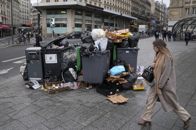 A woman walks past a pile of garbage cans Tuesday, March 7, 2023 in Paris. Garbage collectors, utility workers and train drivers are among people walking off the job Tuesday across France to broadcast their anger at a bill raising the retirement age to 64, which unions see as a broader threat to the French social model. (Photo by Michel Euler/AP Photo)