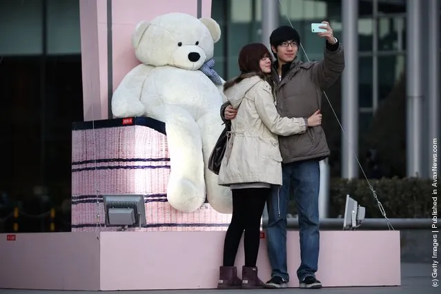A Chinese man takes pictures with his girlfriend posing with a giant teddy bear for Valentine's Day outside a shopping mall