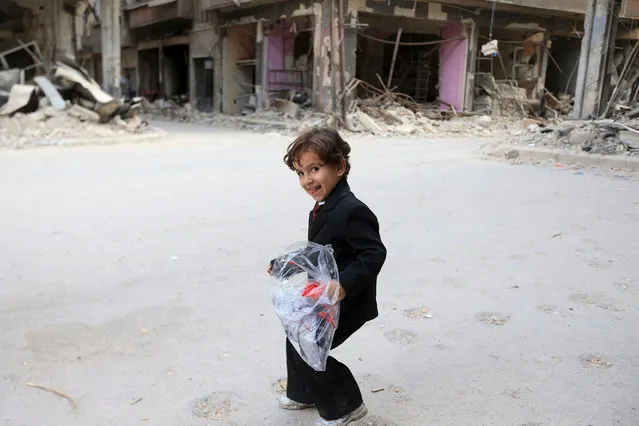 A boy carries a bag of new clothes ahead of the Eid al-Fitr holiday marking the end of Ramadan in Jobar, a suburb of Damascus, Syria July 15, 2015. (Photo by Bassam Khabieh/Reuters)