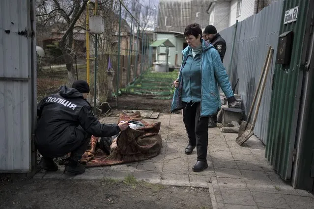 A policeman examines the corpse of a man killed during the war with Russia in Bucha, in the outskirts of Kyiv, Ukraine, Monday, April 11, 2022. (Photo by Rodrigo Abd/AP Photo)