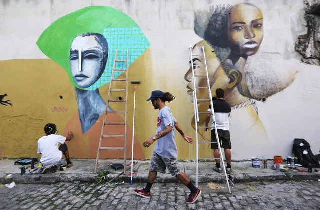 Artists Lucas Ururah (L) and Gil Faria (R) paint graffiti as organizer Hugo Oliveira (C) walks past in the Providencia “favela” community, the oldest favela in Rio, as part of the “Providencia Gallery” project on May 6, 2017 in Rio de Janeiro, Brazil. The artists created an open-air street art gallery in the “favela” to promote local business, tourism and culture at a time when many of Rio's favelas are suffering from a wave of violence amidst a deep recession in Brazil. (Photo by Mario Tama/Getty Images)
