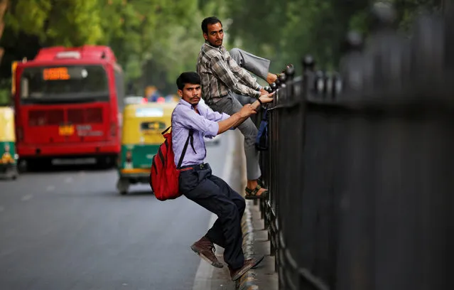 Commuters climb a fence on a road divider to cross a busy road in New Delhi, June 16, 2017. (Photo by Adnan Abidi/Reuters)