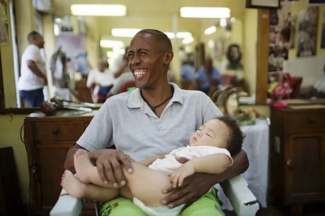 Street vendor Alain Rivera, 37, holds his 10-month-old nephew in a barber shop in downtown Havana, July 14, 2015. (Photo by Alexandre Meneghini/Reuters)