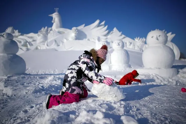 Girls play in front of a snow sculpture for the upcoming Harbin International Ice and Snow Sculpture Festival, in the northern city of Harbin, Heilongjiang province, China on January 3, 2020. (Photo by Aly Song/Reuters)