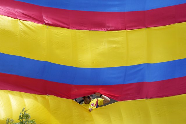 A man looks through an opening of a giant Colombian national flag during the Independence Day military parade, in Bogota, Colombia, Thursday, July 20, 2023. Colombia is marking 213 years of independence from Spain. (Photo by Fernando Vergara/AP Photo)