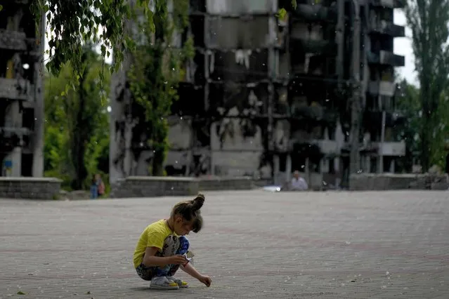A girl plays at a square near buildings destroyed during attacks in Borodyanka, on the outskirts of Kyiv, Ukraine, Saturday, June 4, 2022. (Photo by Natacha Pisarenko/AP Photo)