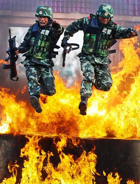 Chinese paramilitary policemen jump through a wall of fire during a training exercise at a military base in Chuzhou, China on July 25, 2012. (Photo by Associated Press)