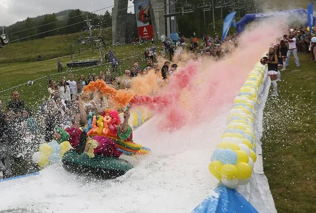 A participant holds smoke flares while sliding down on a float along a chute to cross a pool of water and foam during the “Letniy Gornoluzhnik” (Summer mountain puddle rider) festival at the Bobroviy Log Fun Park near the Siberian city of Krasnoyarsk, Russia, August 23, 2015. (Photo by Ilya Naymushin/Reuters)
