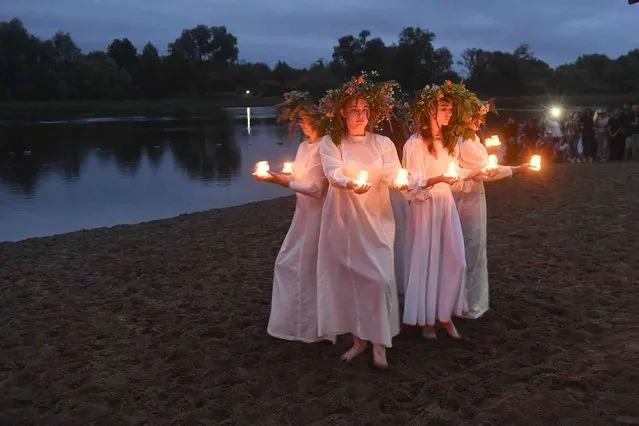 Belarusian girls holding candles stand at the Berezina river on Ivan Kupala Day, an ancient night long celebration marking the Summer Solstice, the shortest night of the year, in Parichi village, some 200 km (125 miles) south of Parichi , Belarus, Wednesday, July 6, 2022. Ivan Kupala or St. John's Day or Midsummer Day, is a traditional carnival, which centers around a bonfire with plenty of food and dancing. (Photo by Viktor Drachev/AP Photo)