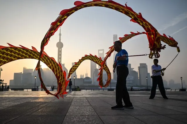Men twirl dragon streamers on the Bund promenade along the Huangpu River during sunrise in Shanghai on September 7, 2022. (Photo by Hector Retamal/AFP Photo)