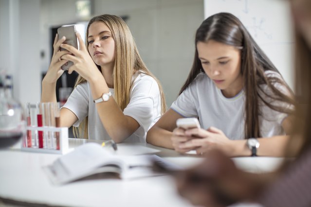 Teenage girls using cell phones in science class. (Photo by Westend61/Getty Images)