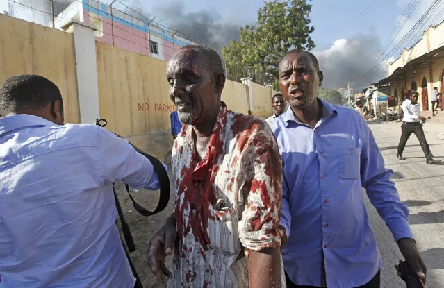 Somalis help a man wounded after a blast in the capital Mogadishu, Somalia Saturday, October 14, 2017. (Photo by Farah Abdi Warsameh/AP Photo)