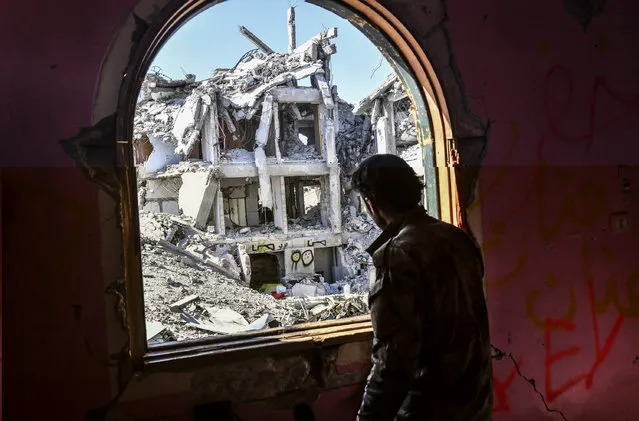 A member of the Syrian Democratic Forces (SDF), backed by US special forces, looks out from a building at the frontline in Raqa on October 16, 2017 in the Islamic State (IS) group jihadist' crumbling stronghold. US-backed fighters battled hundreds of Islamic State group jihadists holed up in the last pockets of Syria's Raqa, as the former extremist stronghold stood on the verge of capture. (Photo by Bulent Kilic/AFP Photo)