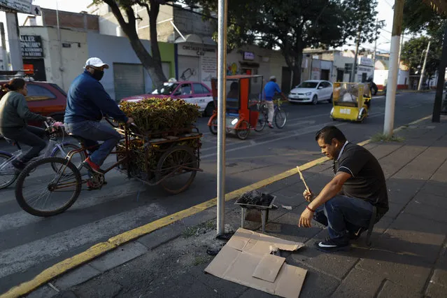Jose Vargas stokes a carbon stove to heat tamales, as part of the street side breakfast stand he has operated for 15 years, with the help of his wife and sons, in the Xochimilco district of Mexico City, Friday, May 15, 2020. Vargas said they respected the stay at home recommendation for two weeks amid the COVID-19 pandemic, before running out of food. “We'll either die of hunger, or of sickness”, Vargas said. (Photo by Rebecca Blackwell/AP Photo)