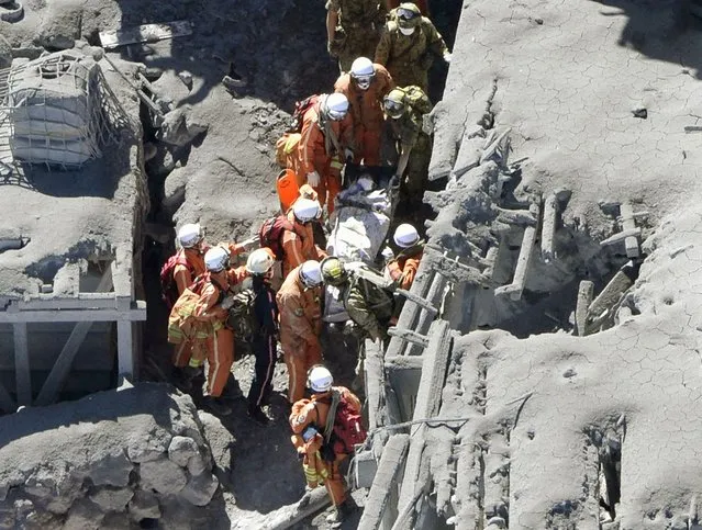 Japan Self-Defense Force (JSDF) soldiers and firefighters carry an injured person among mountain lodges, covered with volcanic ash, near a crater of Mt. Ontake, which straddles Nagano and Gifu prefectures in this September 28, 2014 photo taken and released by Kyodo. (Photo by Reuters/Kyodo News)