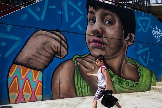 A boy walks in front of a graffiti, portraying a young boy, in Medellin, Colombia on November 19, 2017. (Photo by Juancho Torres/Anadolu Agency/Getty Images)