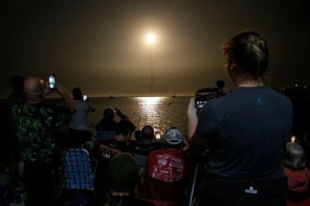 People at Veterans Memorial park watch as the Artemis I unmanned lunar rocket lifts off from launch pad 39B at NASA's Kennedy Space Center, in Titusville, Florida, on November 16, 2022. NASA's Artemis 1 mission is a 25-and-a-half day voyage beyond the far side of the Moon and back. The meticulously choreographed uncrewed flight should yield spectacular images as well as valuable scientific data. (Photo by Marco Bello/AFP Photo)
