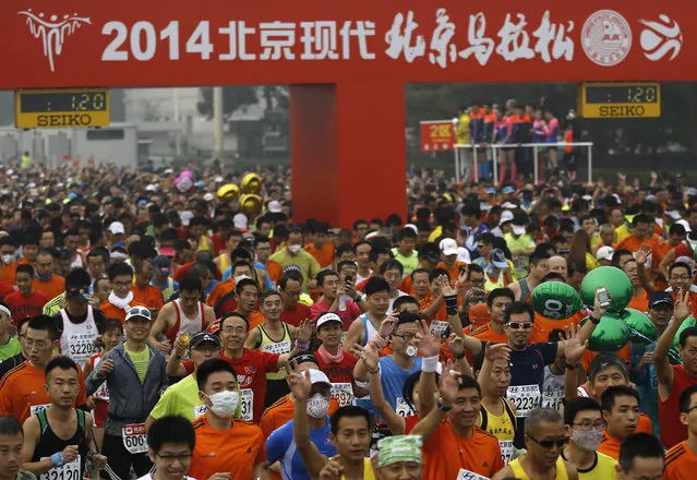 Runners, some wearing masks to protect themselves from pollutants, jog at Tiananmen Square shrouded in haze at the start of 2014 Beijing International Marathon in Beijing, China Sunday, October 19, 2014. (Photo by Andy Wong/AP Photo)