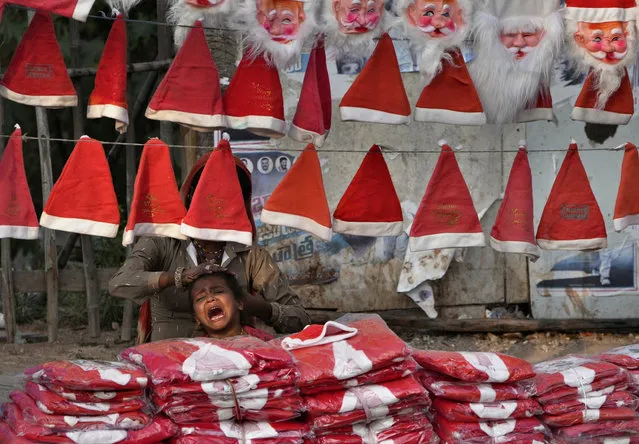 A street vendor selling Santa caps combs her daughter as she waits for buyers ahead of Christmas in Hyderabad, India, Thursday, December 22, 2022. (Photo by Mahesh Kumar A./AP Photo)