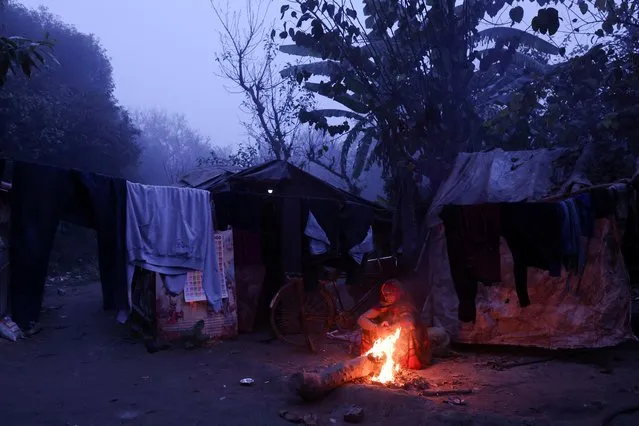 A woman sits next to a bonfire near a nursery on a cold winter morning in New Delhi, India on January 5, 2023. (Photo by Anushree Fadnavis/Reuters)